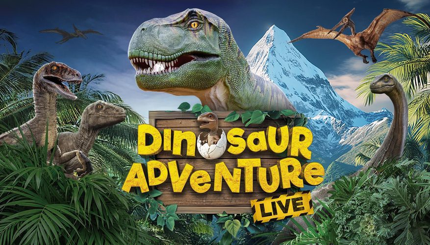 T-Rex in foreground surrounded by trees and mountains in the background.