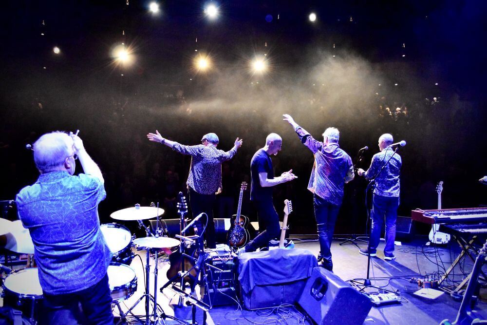 All five band members on stage facing towards the audience away from the camera.