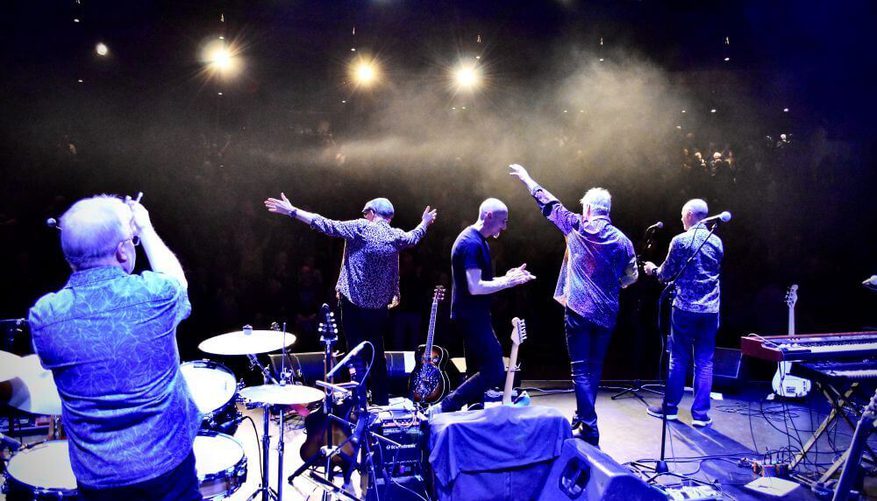 All five band members on stage facing towards the audience away from the camera.
