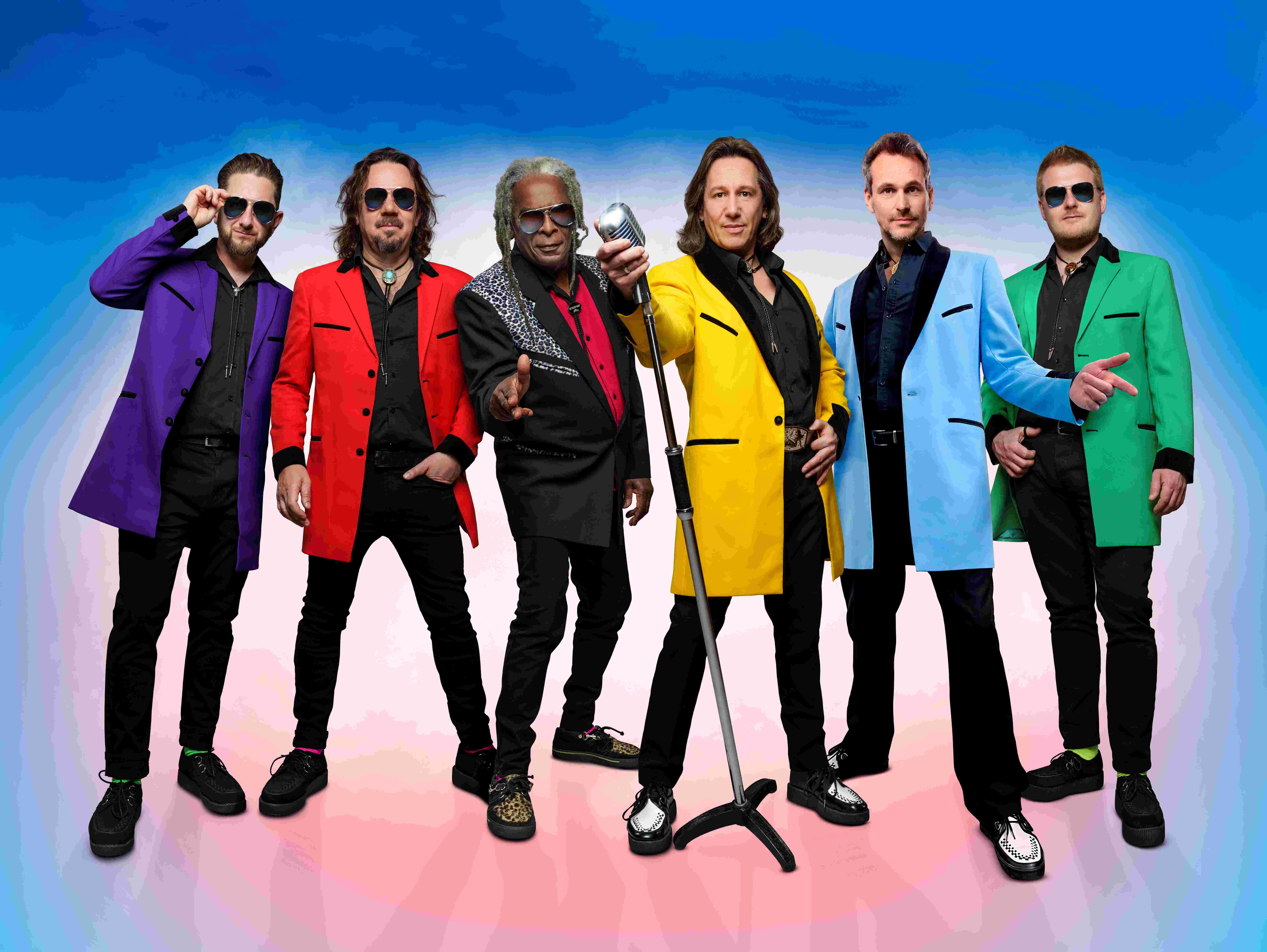 Six men stood in a line all wearing a coloured jacket, black shirt and black trousers.