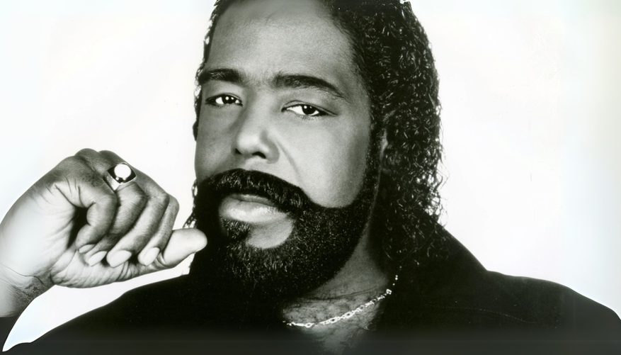 Black and white image of a man with a beard, wearing a black shirt and necklace.