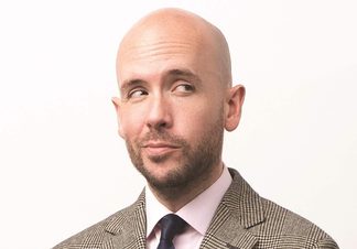 Headshot of Tom wearing a tweed suit, white shirt and navy blue tie.