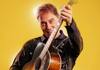 Man poses with an acoustic guitar.